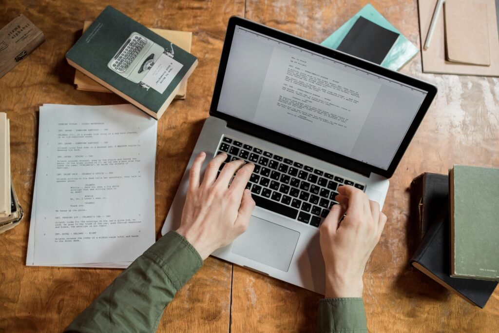 pexels-photo-8035295-8035295 High-angle view of hands typing on a laptop surrounded by books and papers.
